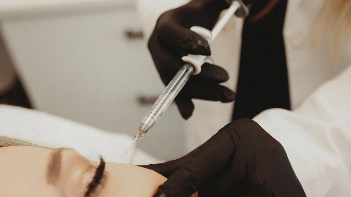 A person in black gloves administers an injection near a patient's eye in a clinical setting. The scene conveys a sense of precision and care.