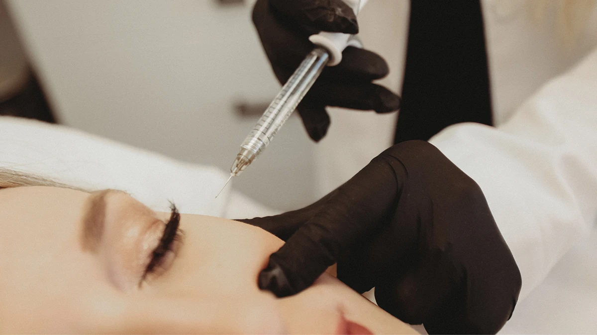 A woman receiving eyebrow shaping from a doctor in a clinical setting.