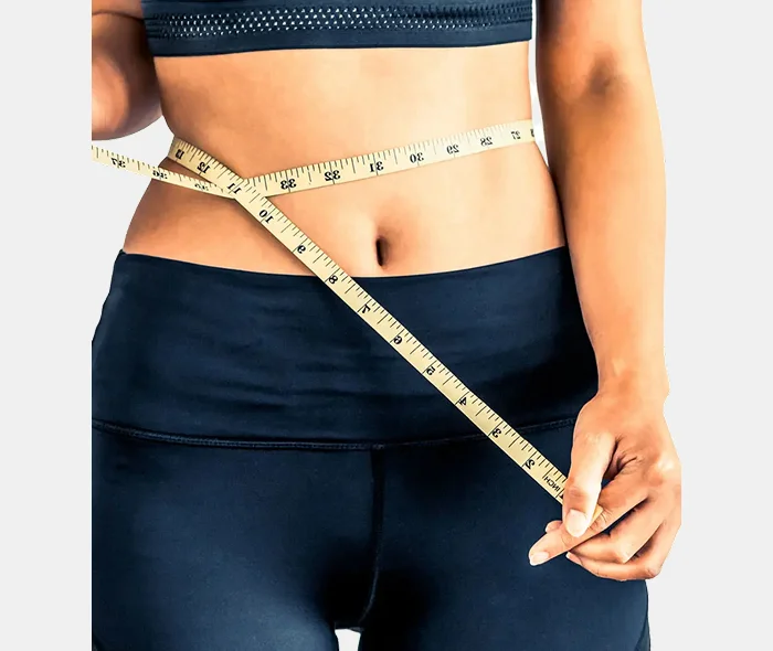 A person in a black sports outfit measures their waist with a tape measure. The focus is on the midsection, emphasizing fitness and health.