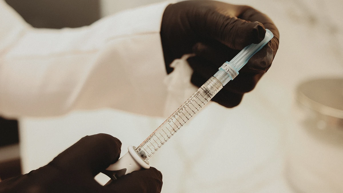 A healthcare professional in a white coat holds a syringe, preparing for a medical procedure or vaccination.