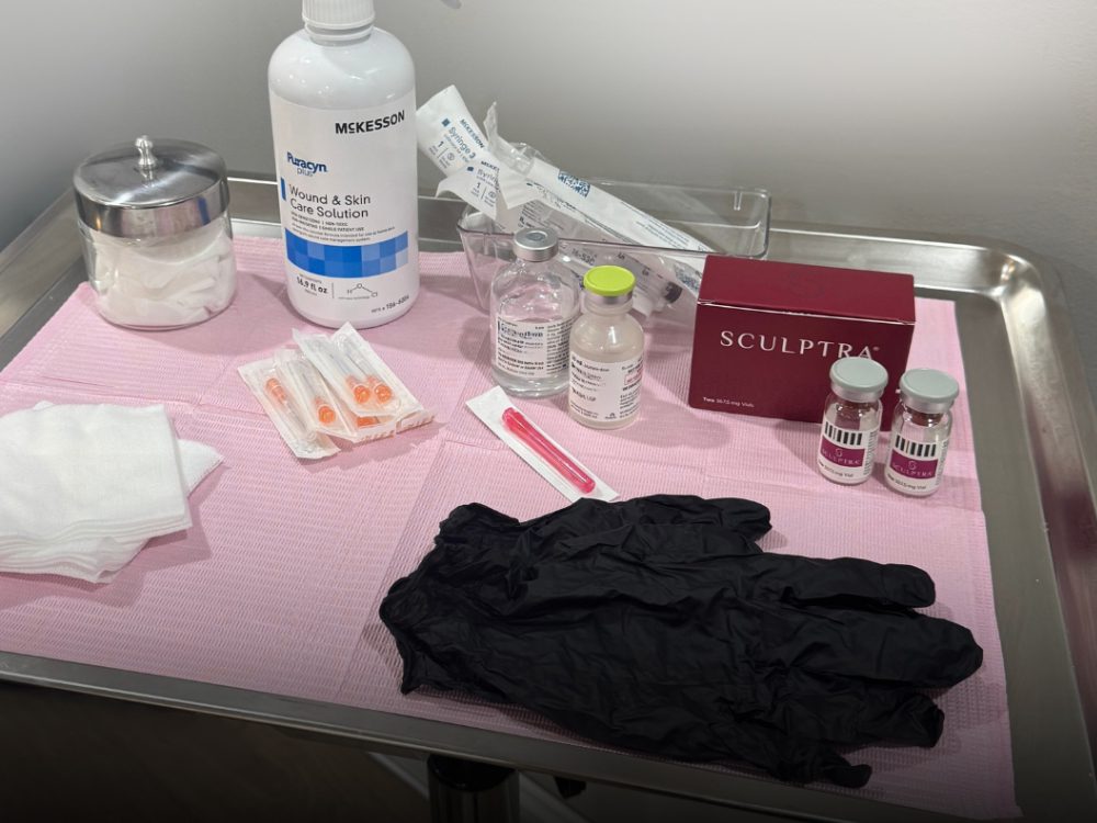 A clinical setup on a tray includes wound care solution, syringes, sealed wipes, black gloves, Sculptra box, and medication vials, conveying a medical, sterile environment.